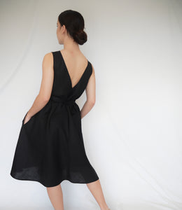 Woman wearing elegant black A-line summer linen ALBA dress with deep v-shaped back line. Side seam pockets with double looping self fabric belt. Australian made