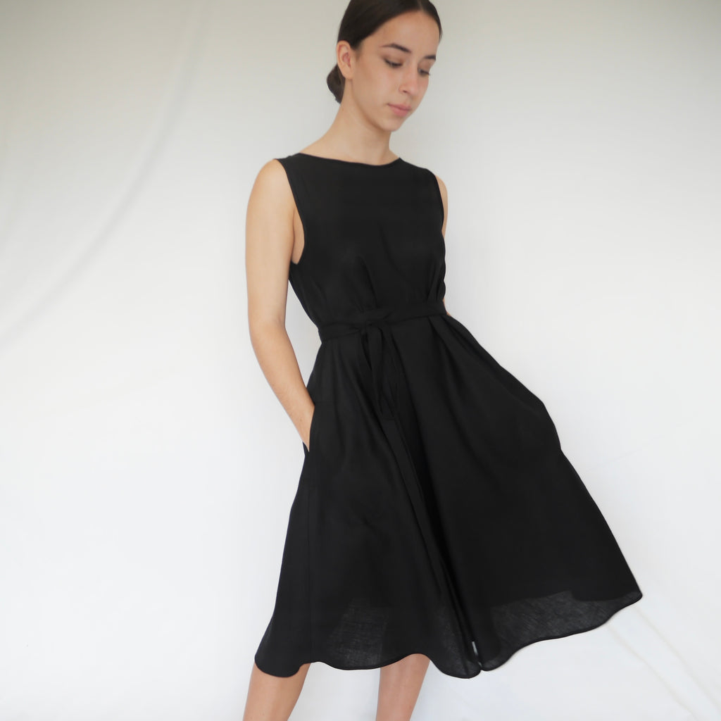 Woman wearing elegant black A-line summer linen ALBA dress with deep v-shaped back line. Side seam pockets with double looping self fabric belt. Australian made.