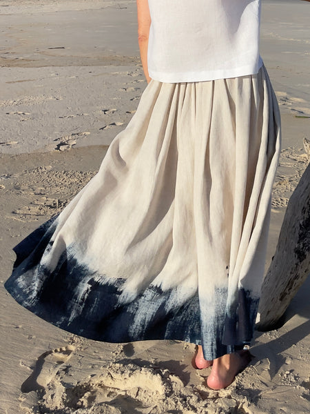 natural linen coloured skirt with elastic waist, lower calf length with dark navy rough painted hem, blowing in breeze.