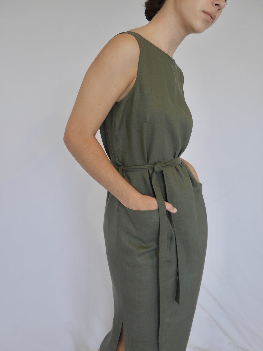 Woman wearing sleeveless NICO  khaki linen straight mid-calf length summer dress. Front pockets, self tie belt, side splits. Australian made