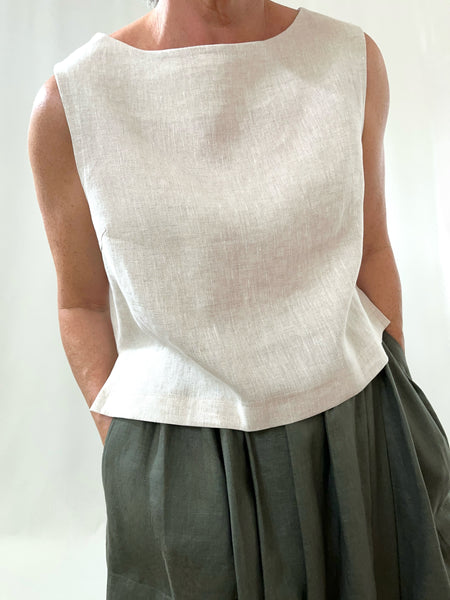 woman wearing a cream linen sleeveless top and khaki skirt against a plain background
