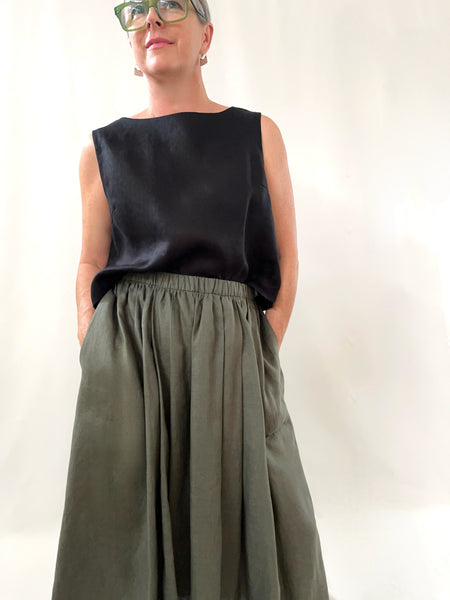 Person wearing a black linen sleeveless top tucked into a khaki skirt against a plain background
