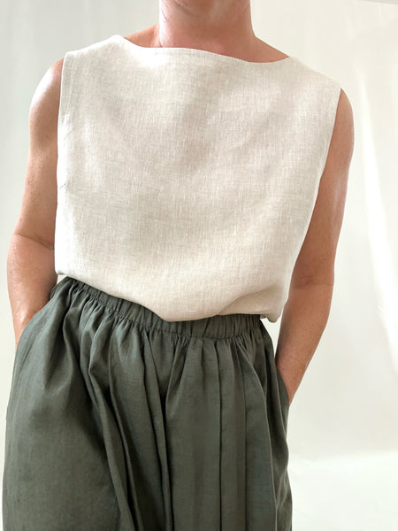 Person wearing a cream linen sleeveless top and khaki skirt against a plain background