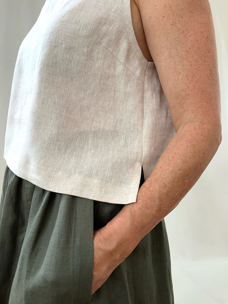 woman wearing a cream linen sleeveless top and khaki skirt against a plain background