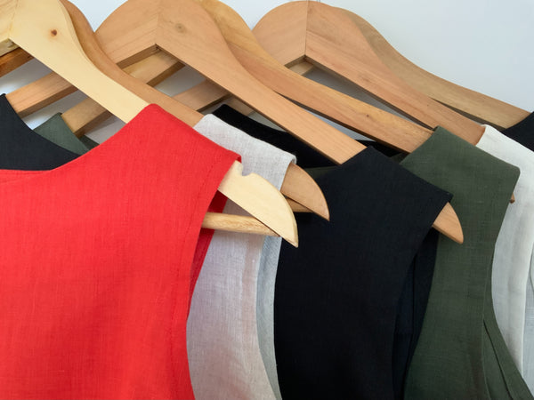 Red, black, white, khaki and cream linen  tops on wooden hangers against a white background