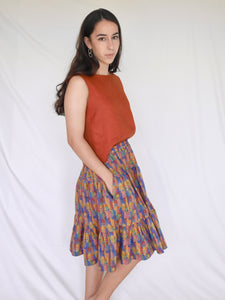 Woman wearing 3 tiered cotton printed skirt, knee length, elastic waisted with voluminous hem in mulitcoloured Copenhagen houses print. Colours are blue, rust red, mustard yellow, green.