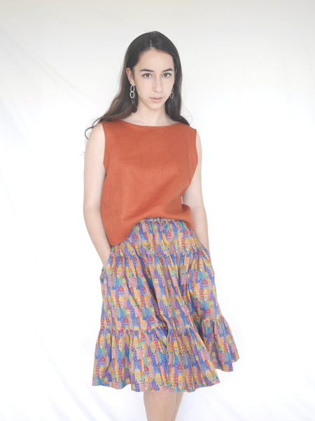 Woman wearing 3 tiered cotton printed skirt, knee length, elastic waisted with voluminous hem in mulitcoloured Copenhagen houses print. Colours are blue, rust red, mustard yellow, green.