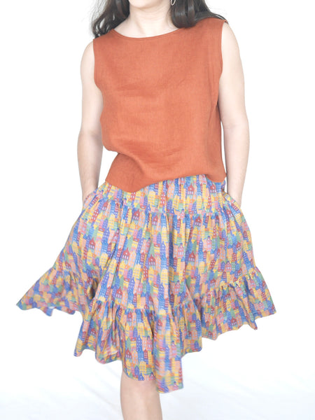 Woman wearing 3 tiered cotton printed skirt, knee length, elastic waisted with voluminous hem in mulitcoloured Copenhagen houses print. Colours are blue, rust red, mustard yellow, green.