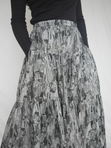 Woman wearing 3 tiered cotton black and white printed skirt, mid calf length, elastic waisted with voluminous hem. Side pockets