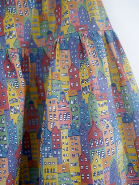 Close up of 3 tiered cotton printed skirt, knee length, elastic waisted with voluminous hem in mulitcoloured Copenhagen houses print. Colours are blue, rust red, mustard yellow, green.