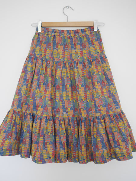 Front on flat view of 3 tiered cotton printed skirt, knee length, elastic waisted with voluminous hem in mulitcoloured Copenhagen houses print. Colours are blue, rust red, mustard yellow, green.